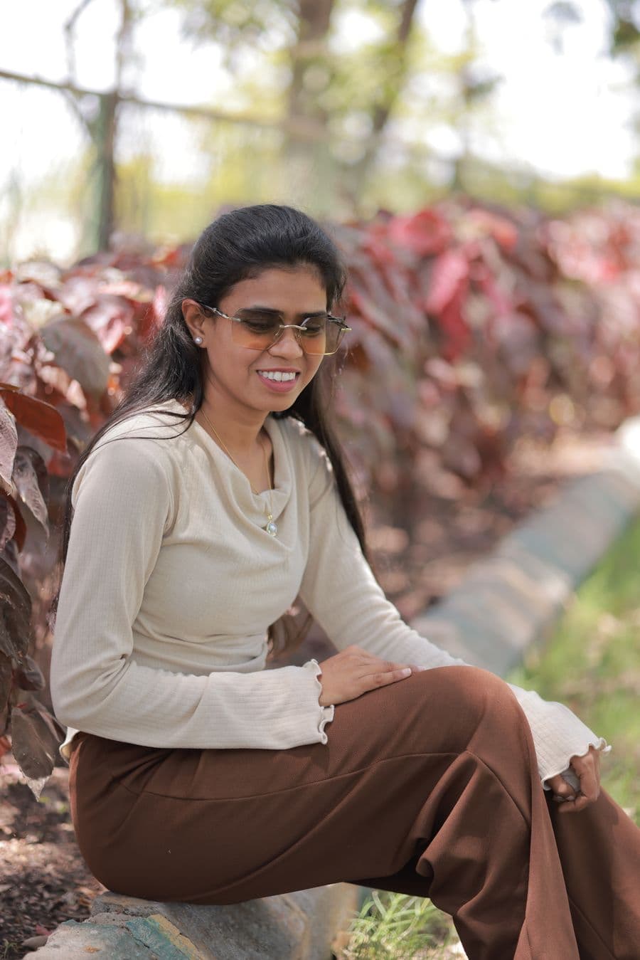 Woman in a cream casual top and brown trousers seated outdoors
